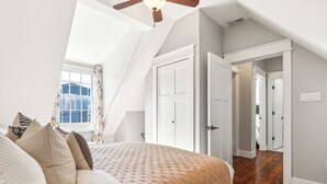 Une chambre avec un grand lit, un ventilateur de plafond et une fenêtre avec des rideaux.
