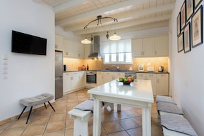A modern kitchen with white cabinets, a central island, and a bench seating area. - Thea Estate (Kassopei)