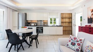 Una cocina moderna con armarios blancos, un refrigerador de acero inoxidable y un comedor con sillas negras y una mesa redonda.
