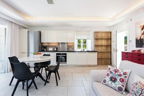 A modern kitchen with white cabinets, a stainless steel refrigerator, and a dining area with black chairs and a round table. - Thea Estate (Kassopei)