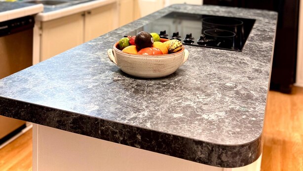 Une cuisine avec un plan de travail en granit, un saladier rempli de fruits et un réfrigérateur noir.