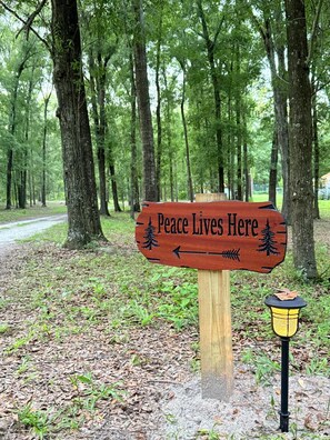 Un panneau en bois portant l’inscription « La paix règne ici » et des flèches indiquant la direction, le tout entouré d’arbres et bordé d’un sentier.