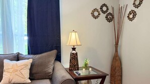 Un salon avec un canapé gris, une petite table sur laquelle se trouve une lampe, des miroirs décoratifs accrochés au mur et un grand vase contenant des branches.