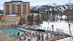 A hotel with a pool area, outdoor seating, and a view of snow-covered mountains. - Main Street Station Suite - Ski-In, Ski-Out, Pool, Hot Tub (Breckenridge)