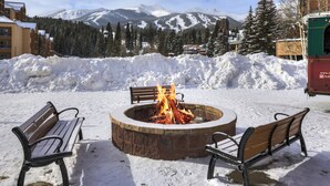 A snow-covered outdoor area with a circular fire pit, two benches, and a mountain backdrop. - Main Street Station Suite - Ski-In, Ski-Out, Pool, Hot Tub (Breckenridge)