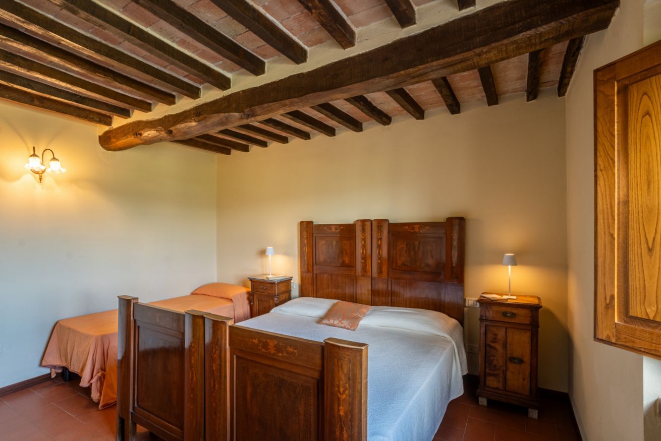 Ein Schlafzimmer mit einem hölzernen Bett, zwei Nachttischen, einem Beistelltisch und einer Holzbalkendecke.