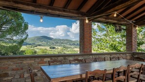 Un'area pranzo esterna rustica con un muro in pietra, tavolo e sedie in legno.