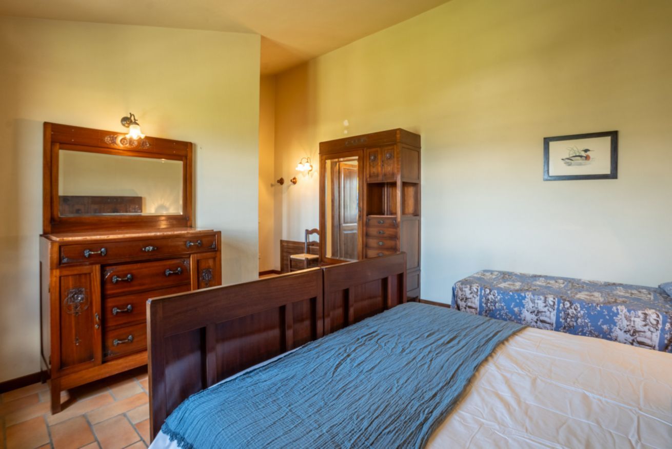 Un dormitorio con cómoda de madera, espejo, cama con manta azul y lámpara de pared.