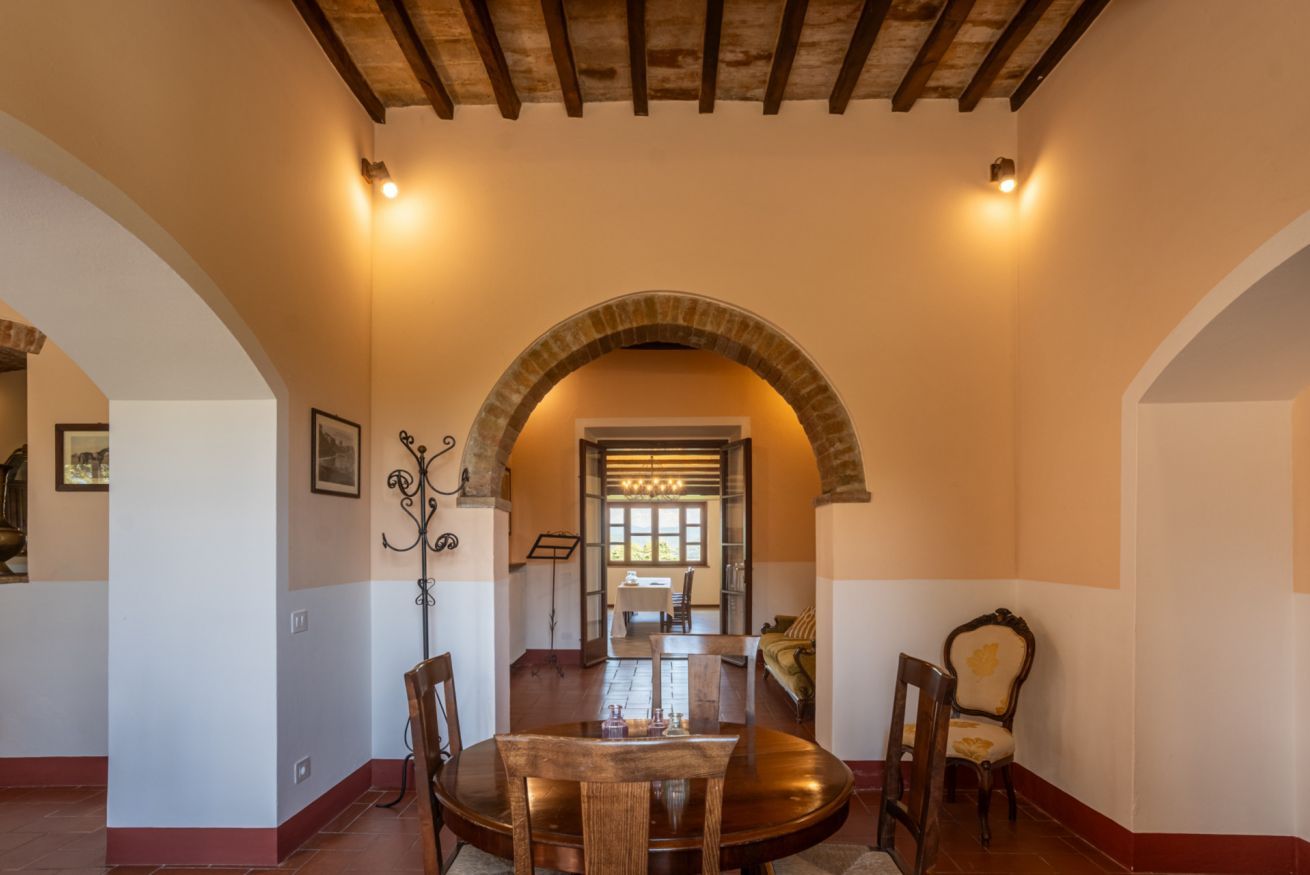 Un espace de salle à manger en forme d’arche, avec une table ronde et des chaises, un lustre et une vue sur une autre salle à manger.