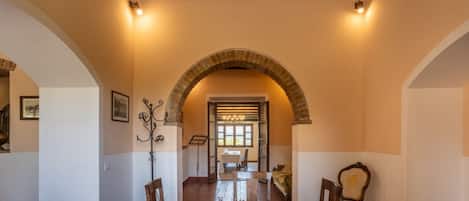 An arched dining area with a round table and chairs, a chandelier, and a view into a dining room.