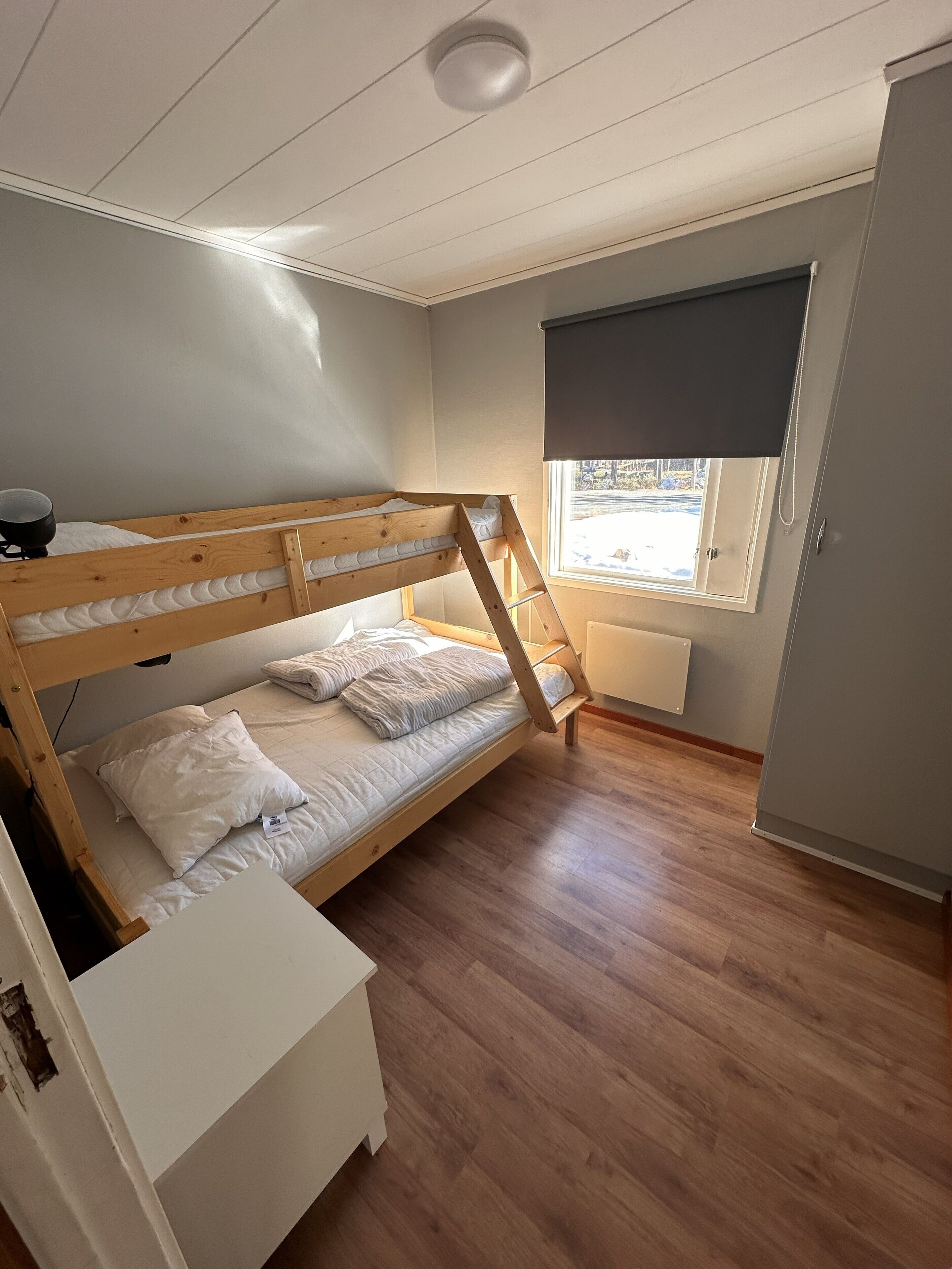 A bunk bed room with a window, a radiator, and a white cabinet.