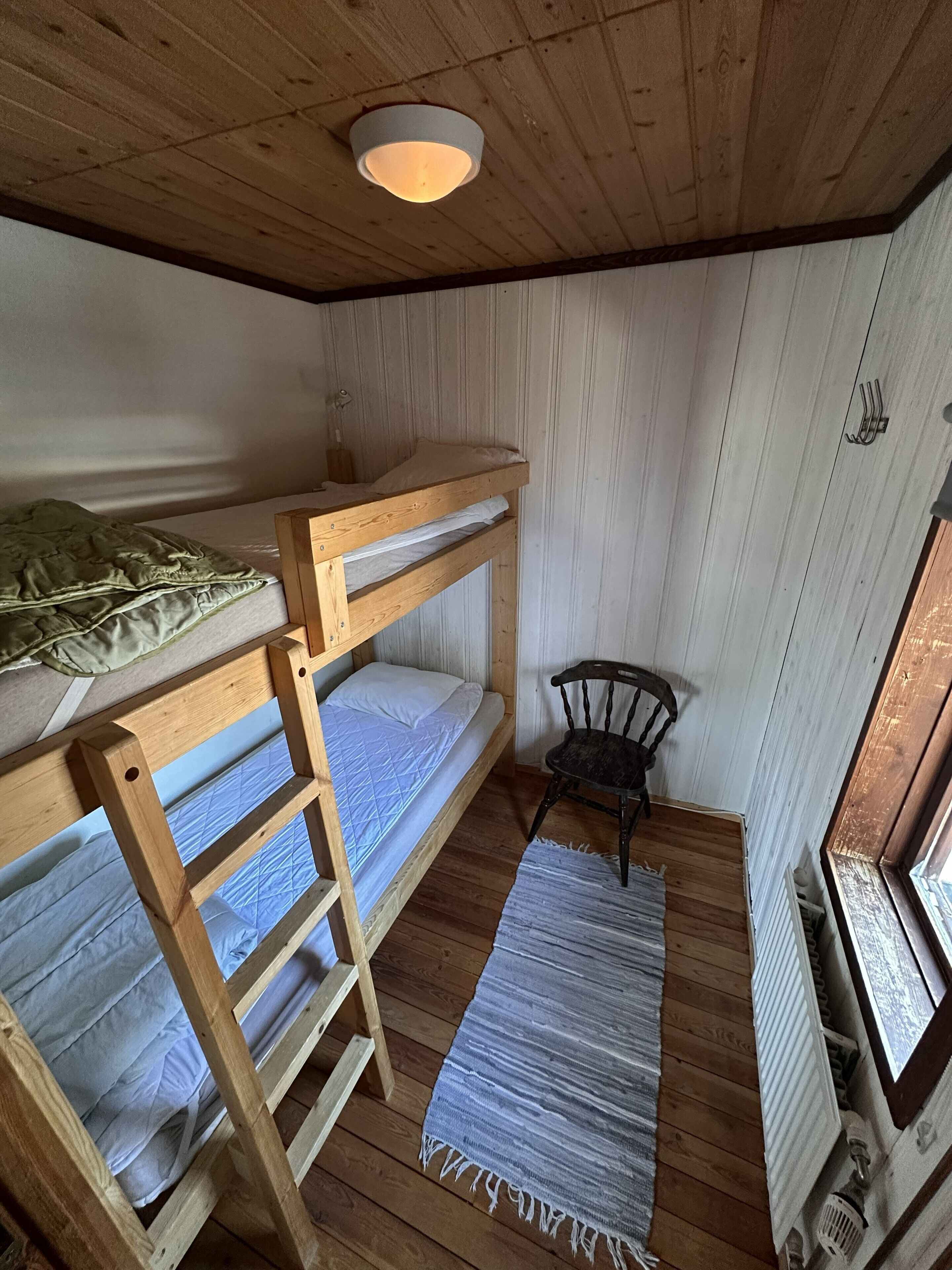 A bunk bed room with a wooden ceiling, a small chair, and a radiator.