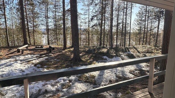 A wooden deck with a railing overlooking a forested area with snow on the ground. - Skabram Camping & Stugby (Jokkmokk)