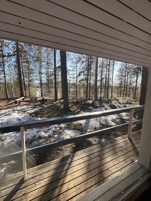 Een houten terras met een reling dat uitkijkt over een bebost gebied met sneeuw.