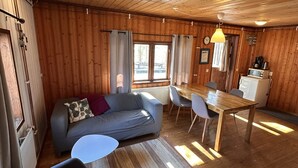 A wooden cabin interior with a sofa, chairs, a dining table, and a kitchen area. - Skabram Camping & Stugby (Jokkmokk)