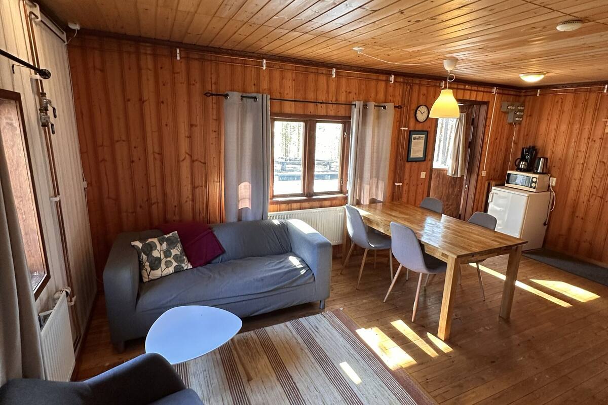 Ein Holzblockhaus-Innenraum mit einer Couch, Sesseln, einem Esstisch und einer Küchenzeile.
