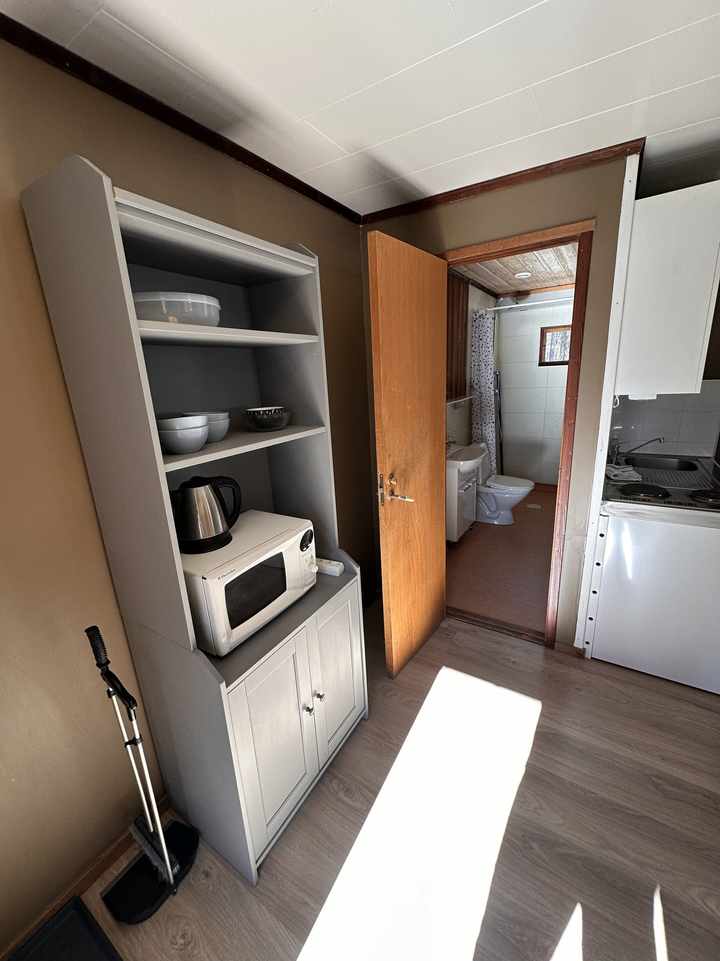A compact kitchen with a microwave, kettle, and cabinets, leading to a bathroom with a toilet and shower.