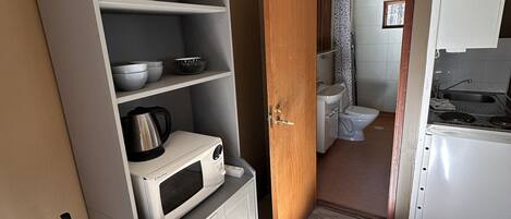 A compact kitchen with a microwave, kettle, and cabinets, leading to a bathroom with a toilet and shower.