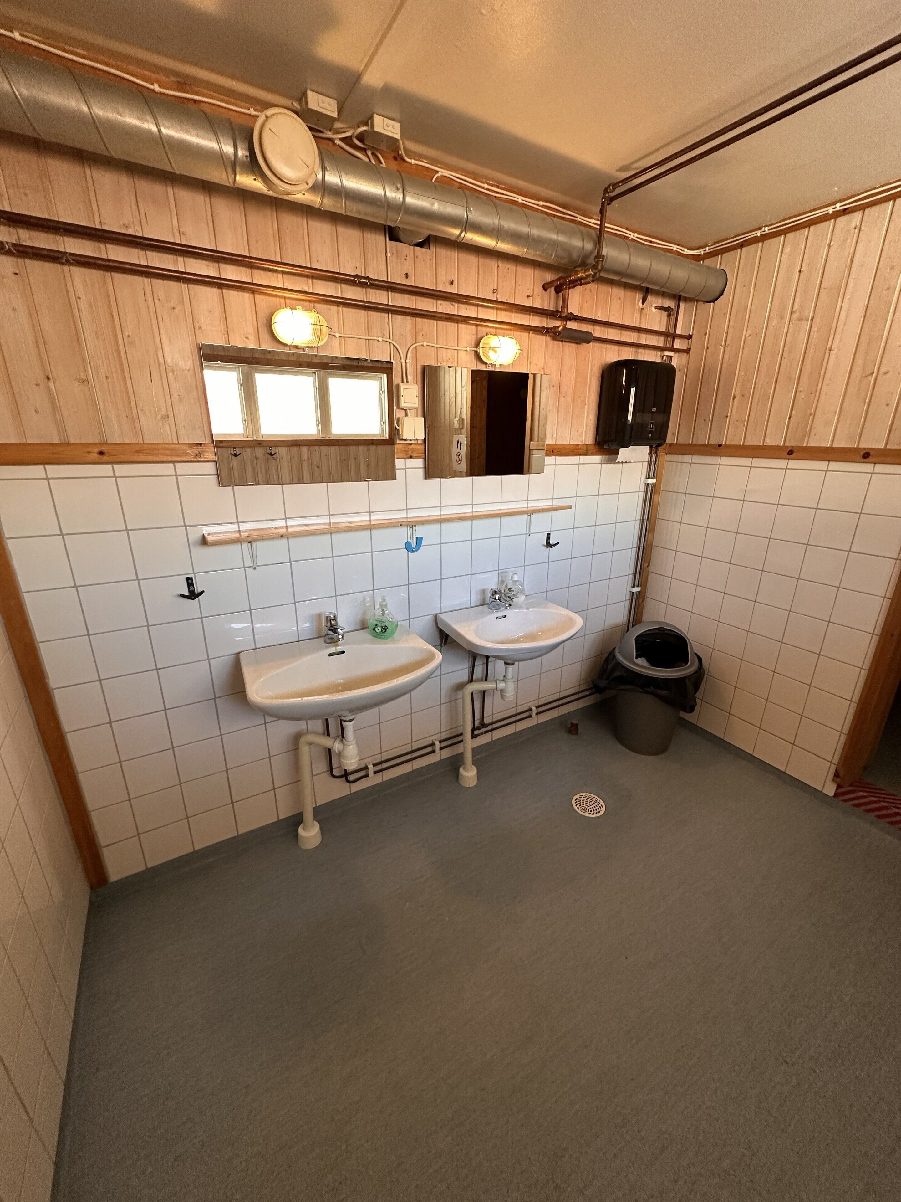 A bathroom with two sinks, a mirror, and a trash can.