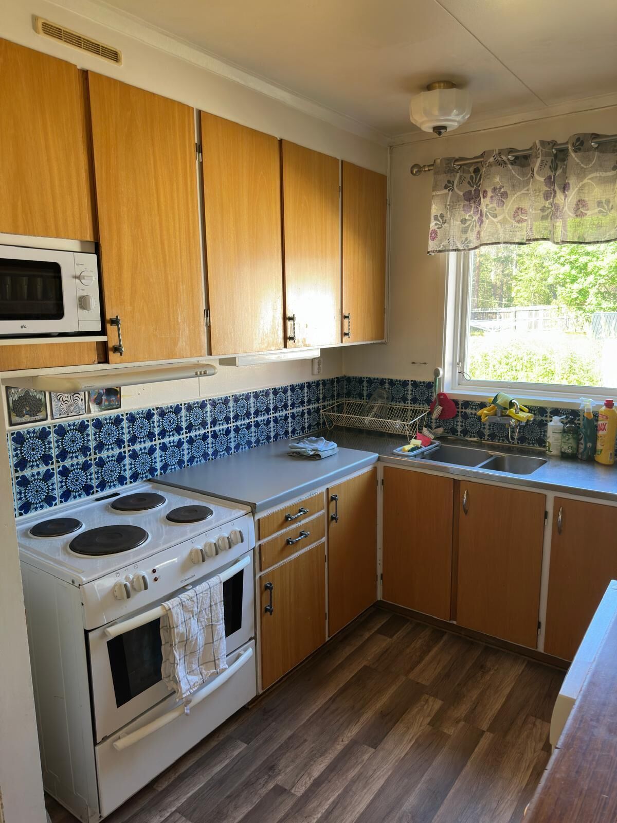 A kitchen with wooden cabinets, a stove, a microwave, and a window with a view.