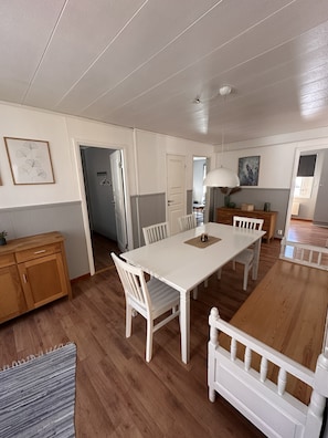 Un vaste espace dédié à la salle à manger, avec une longue table blanche, des chaises blanches et un buffet en bois.