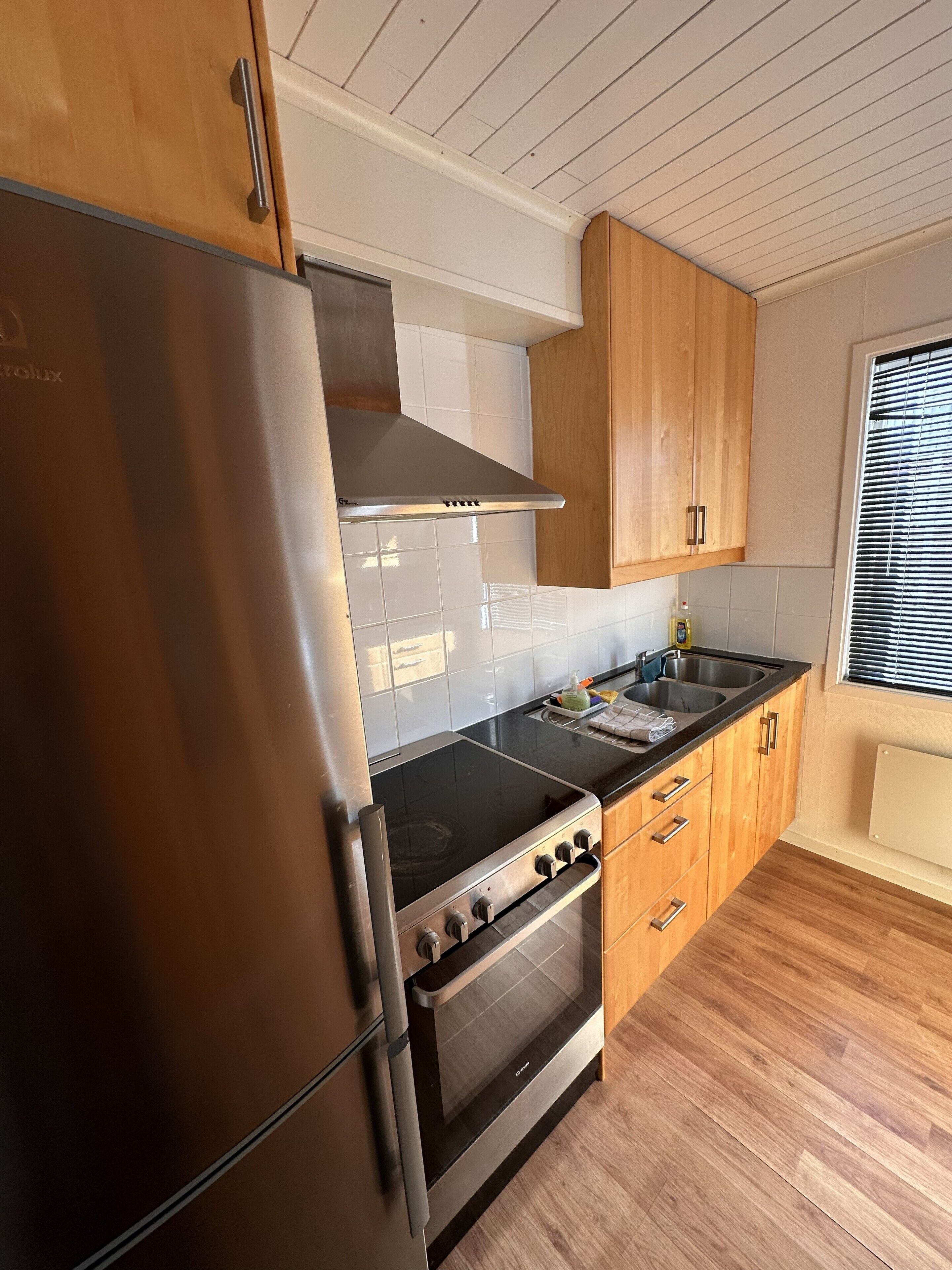 Una cocina con un refrigerador de acero inoxidable, una estufa, armarios de madera y una ventana con persianas.