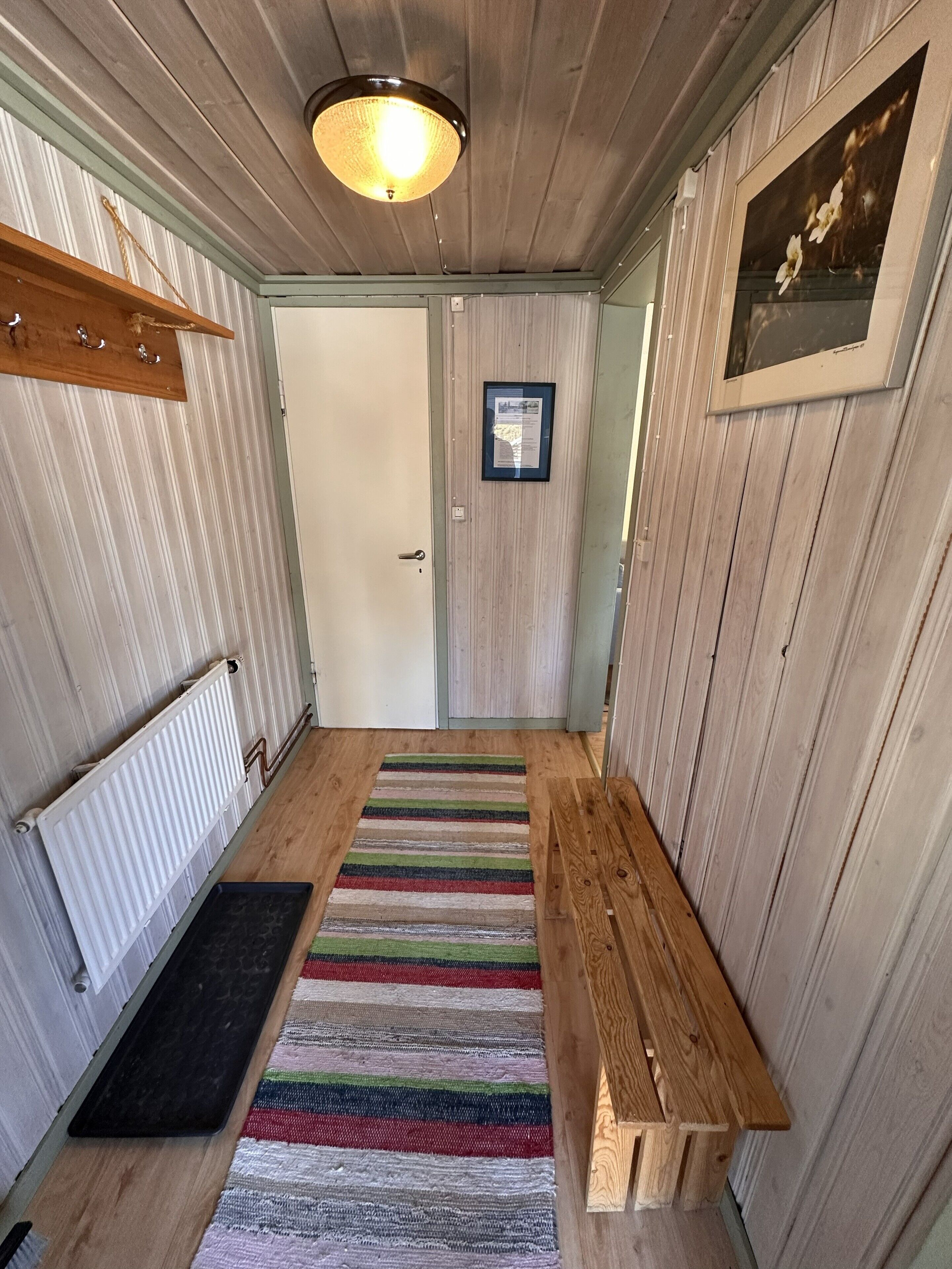 A hallway with a wooden bench, a striped rug, a radiator, and a door with a framed notice.