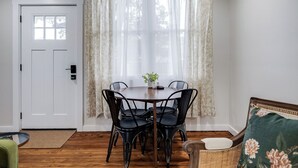 Un coin repas comprenant une table ronde, quatre chaises, une porte et une fenêtre ornée de rideaux légers.