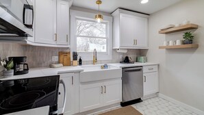 Une cuisine moderne avec des meubles blancs, une cuisinière encastrée, un lave-vaisselle et des étagères en bois au-dessus du plan de travail.