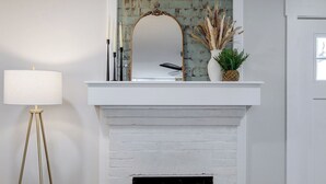 Une cheminée blanche avec un miroir au-dessus, un lampadaire sur le côté gauche et un vase contenant des plantes séchées sur le manteau de la cheminée.