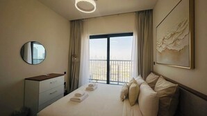 A hotel room with a large bed, a bedside table, a mirror, a window with a view, and a painting on the wall. - Burj Khalifa Views & Lagoonfront Luxury Apartment (Dubai)