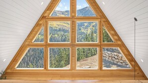 Une pièce dotée d’une grande fenêtre triangulaire qui offre une vue sur une montagne boisée.