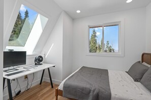 Une chambre à coucher avec un lit, un bureau avec un ordinateur et une fenêtre donnant sur des arbres.