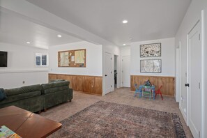 A spacious living room with a green sofa, a wooden accent wall, and a large patterned rug. - Sleeps 15, Stunning A-Frame Retreat with Jaw Dropping Views (Mount Pleasant)