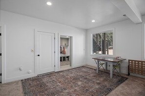 A spacious room with a large window, a wooden table, and a patterned rug.
