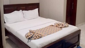 A bedroom with a bed, a wooden headboard, a patterned throw blanket, and a blue rug. - AYEBA ZION HOTEL (Fort Portal)