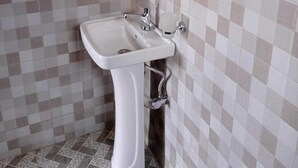A bathroom with a checkered tile wall, a pedestal sink, and a mirror. - AYEBA ZION HOTEL (Fort Portal)