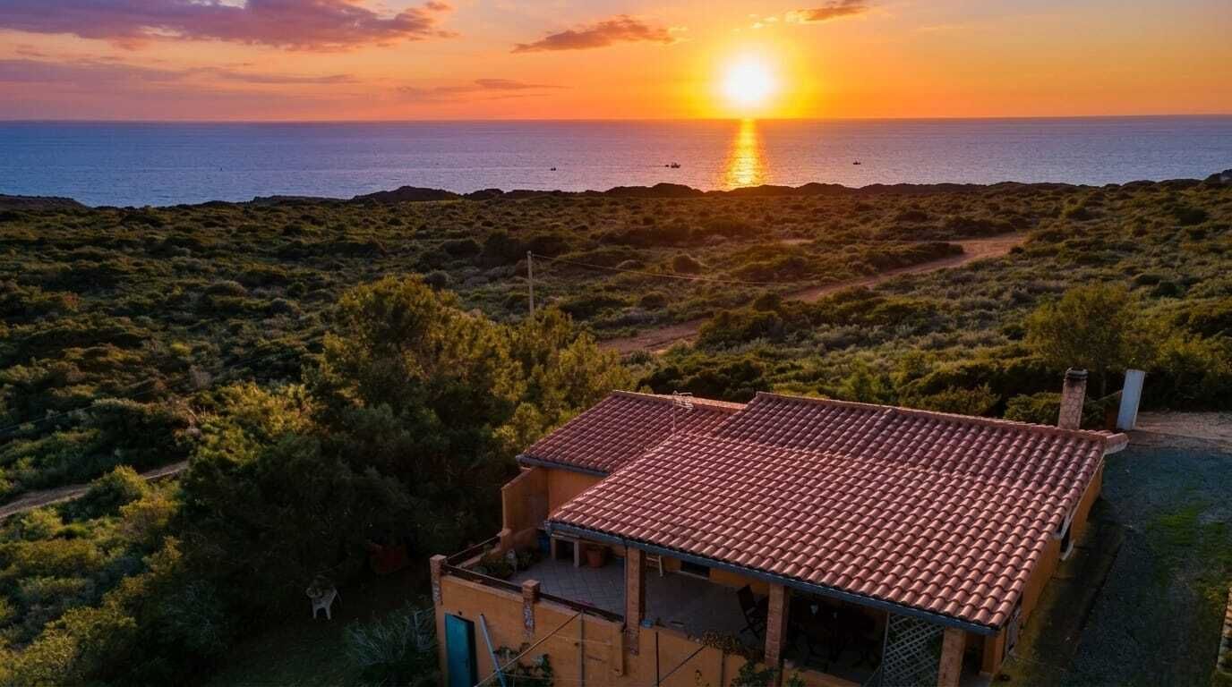 Una propietat costanera amb un edifici de teulada a mosaic, envoltada de vegetació densa i vista al mar al capvespre.