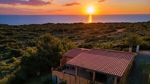 A coastal property with a tiled-roof building, surrounded by dense vegetation and a view of the sea at sunset. - Vacation House a few steps from the sea, Sant'Antioco  (SU)