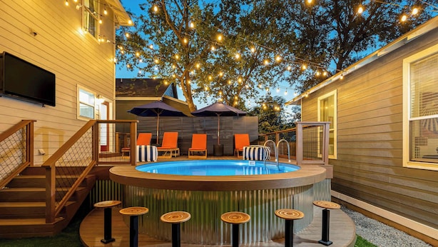 Un jacuzzi con terraza de madera, rodeado de sillas naranjas y una zona de bar con taburetes.