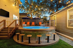 A hot tub with a wooden deck, surrounded by orange chairs and a bar area with stools. - The Backyard Collective - 6BR 2 Homes, Pool & More (Austin)