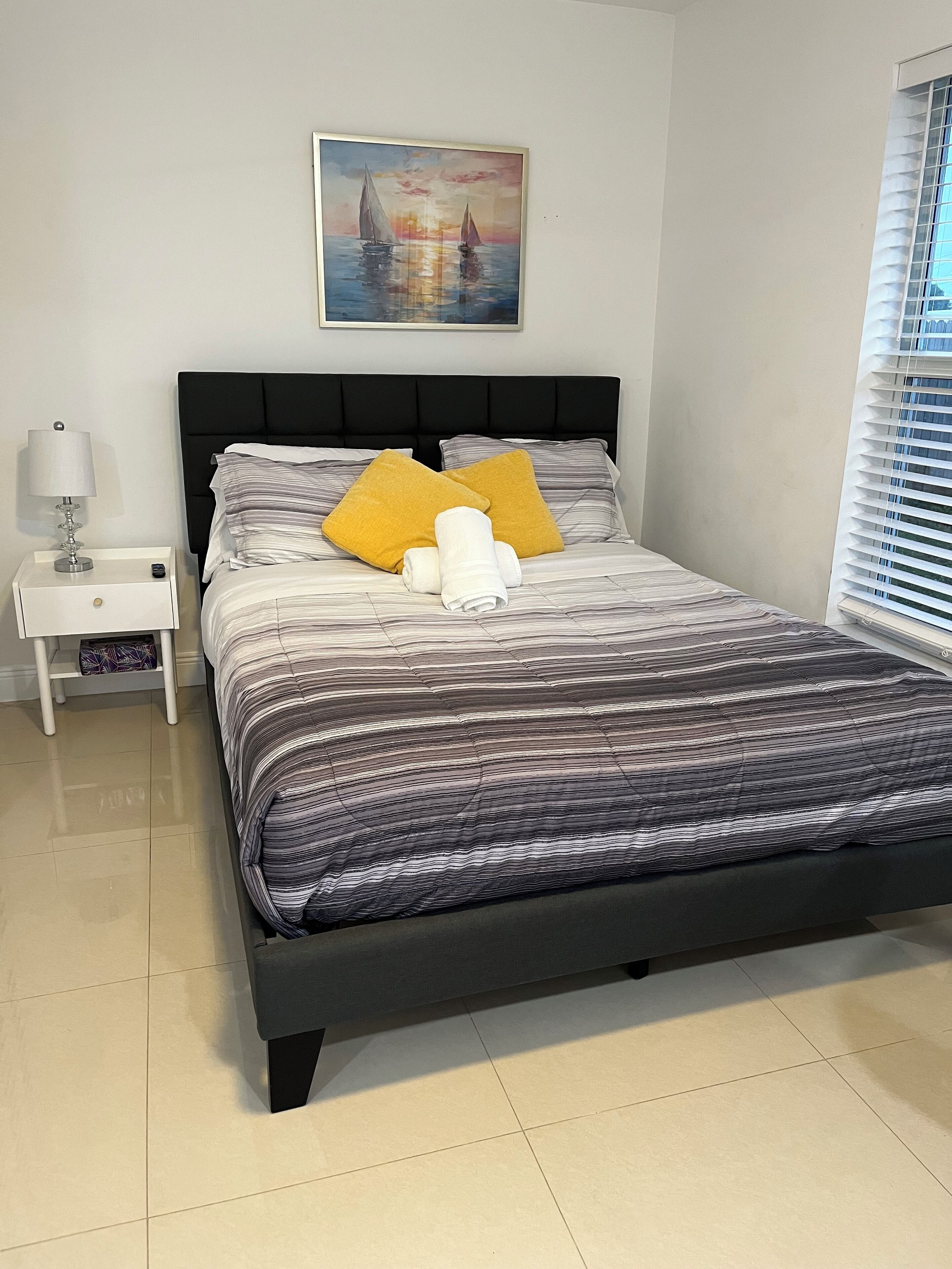 A neatly made bed with striped bedding, two pillows, and rolled towels.