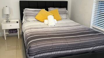 A neatly made bed with striped bedding, two pillows, and rolled towels.