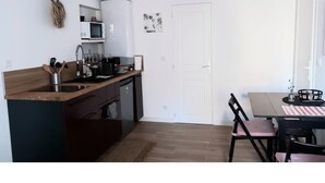 Cozinha compacta com micro-ondas, pia e bancada de madeira. Possui área de refeições com mesa e cadeiras.