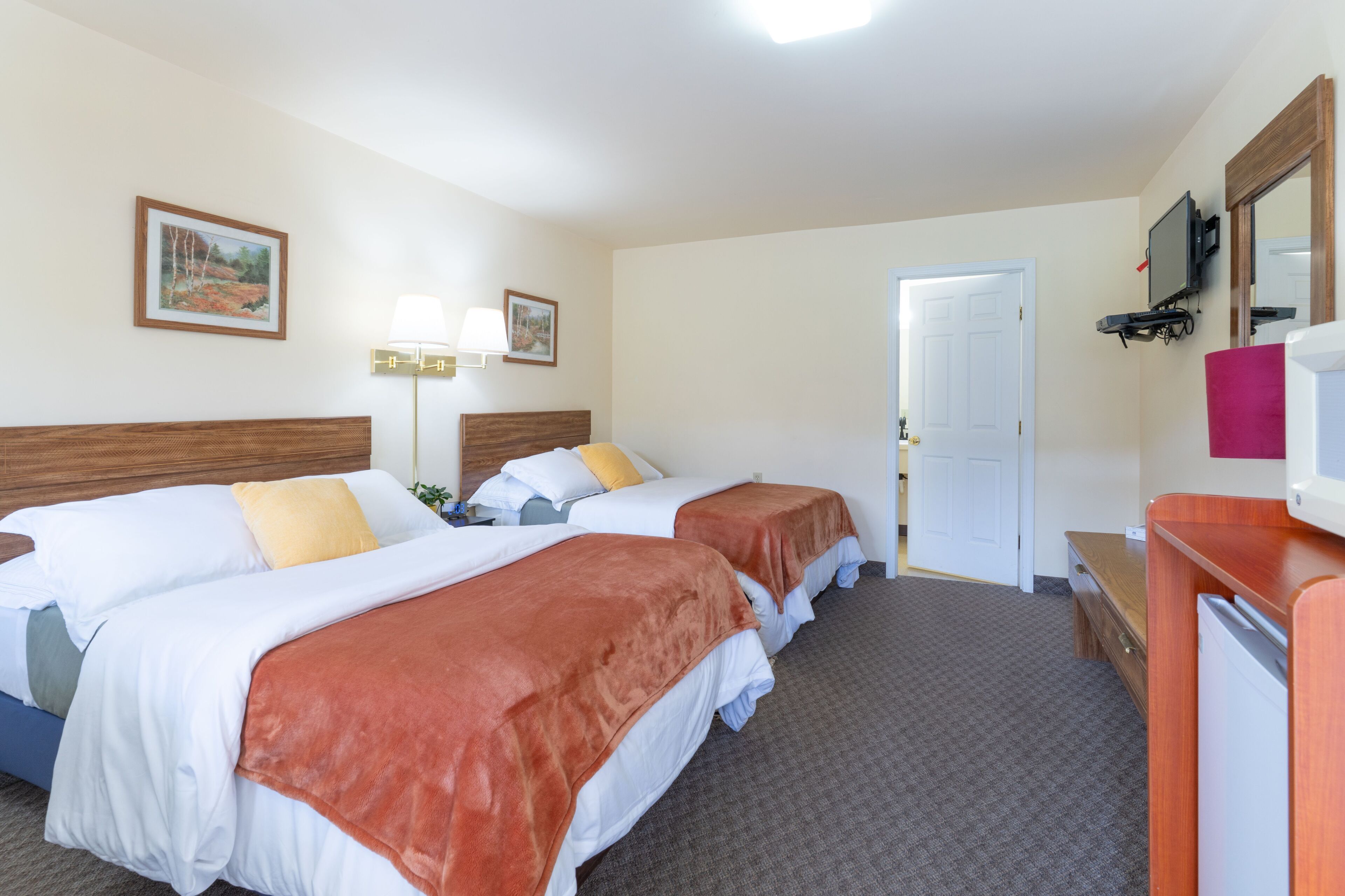A hotel room with two beds, a desk, a TV, and a door leading to another room.