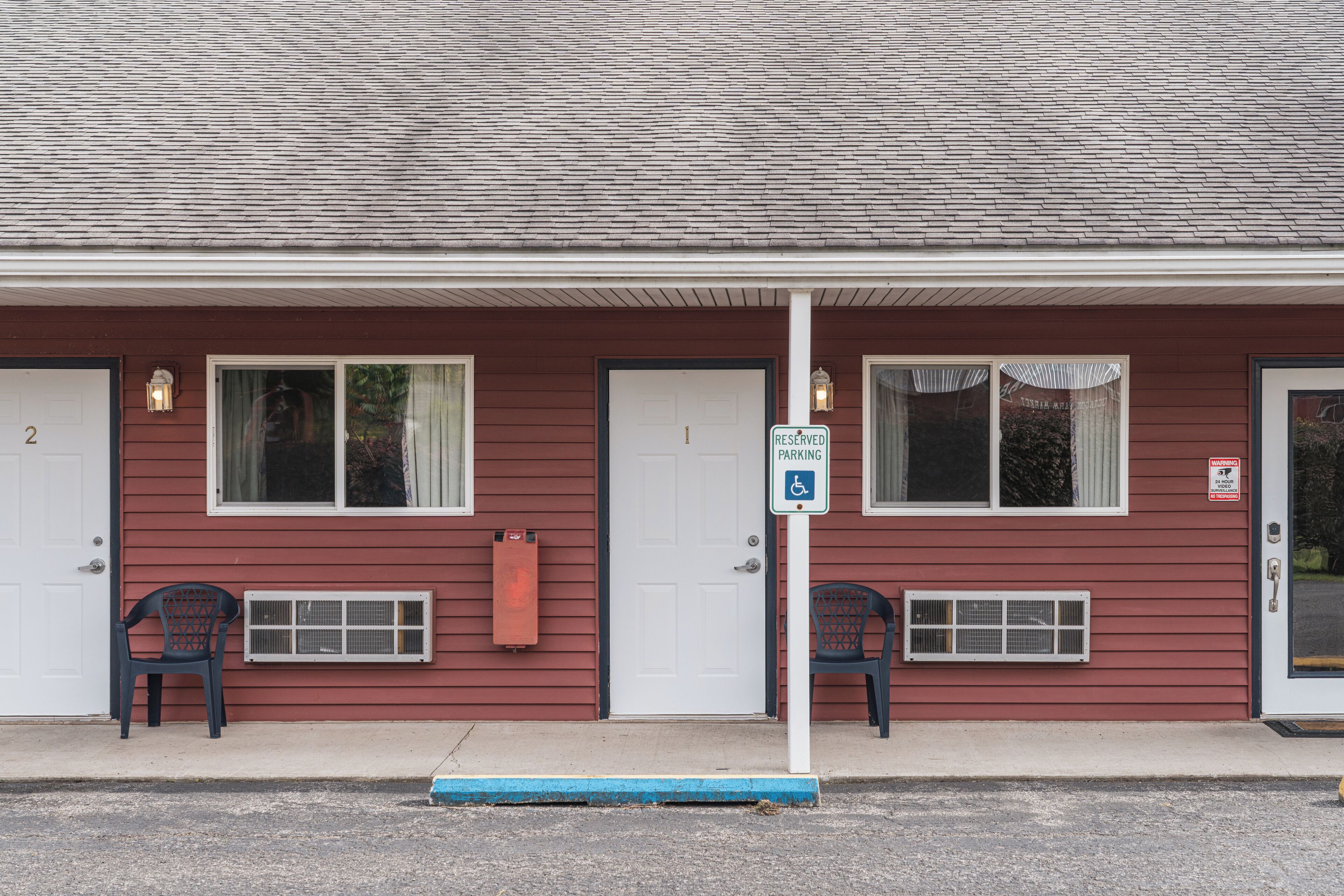 A building with a red exterior, white doors, and windows with curtains. There is a sign indicating reserved parking.