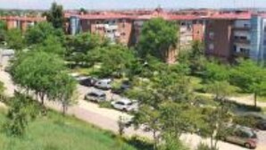 A residential area with multi-story buildings, a parking lot, and greenery.