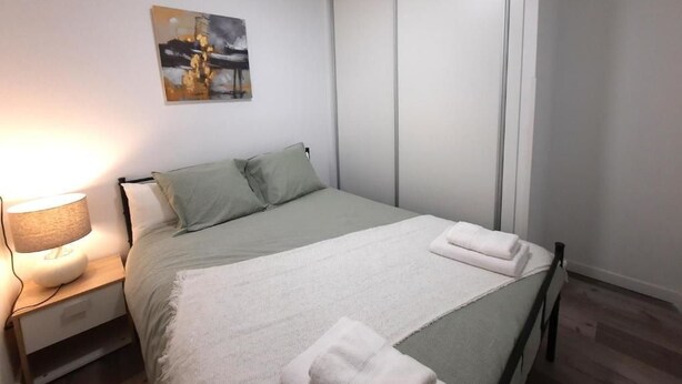 A bedroom with a bed, a nightstand, a lamp, a painting, and a sliding door.