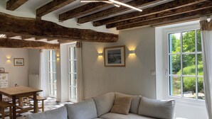 A modern living room with a large L-shaped sofa, wooden beams on the ceiling, and a view of greenery outside. - Mill on the banks of the Indre in Berry. A bucolic, historic site on an island (Ardentes)