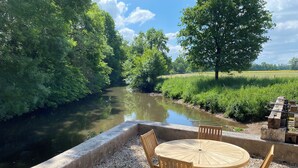 A riverside outdoor seating area with a round wooden table and chairs, surrounded by pebbles and greenery. - Mill on the banks of the Indre in Berry. A bucolic, historic site on an island (Ardentes)
